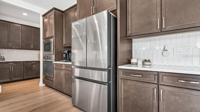 kitchen featuring stainless steel appliances, dark brown cabinets, tasteful backsplash, and light wood-type flooring