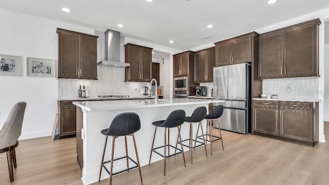kitchen featuring a breakfast bar, wall chimney exhaust hood, a sink, light wood finished floors, and stainless steel appliances