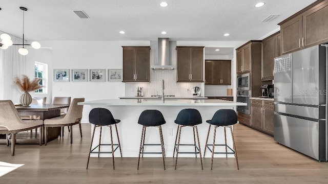 kitchen featuring light countertops, wall chimney exhaust hood, a kitchen breakfast bar, and stainless steel appliances
