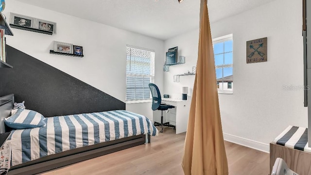 bedroom featuring baseboards, multiple windows, and wood finished floors