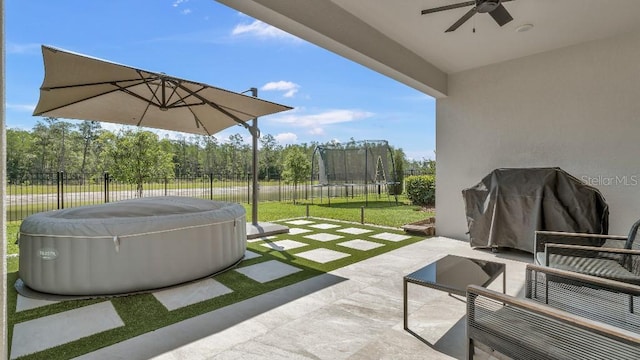 view of patio featuring a ceiling fan, a trampoline, a hot tub, and a fenced backyard
