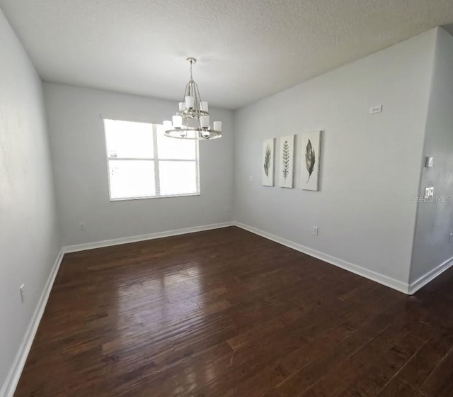 empty room with dark wood-type flooring, baseboards, and a notable chandelier