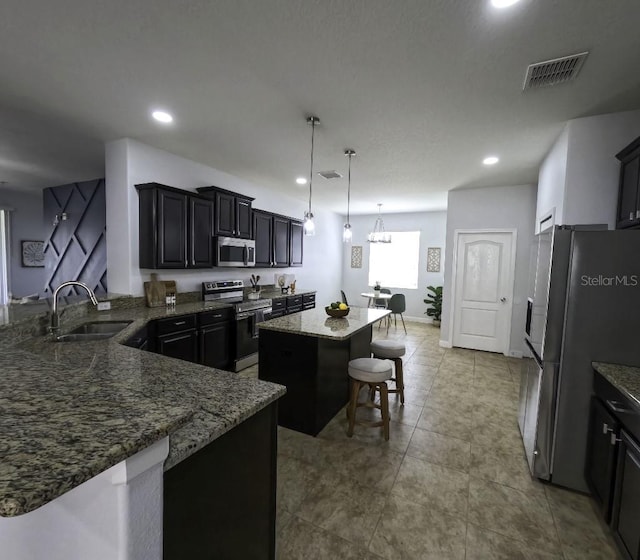 kitchen with visible vents, a center island, dark stone counters, a sink, and appliances with stainless steel finishes