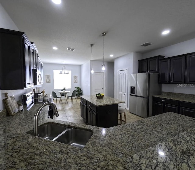 kitchen featuring visible vents, dark cabinetry, a sink, stone counters, and appliances with stainless steel finishes