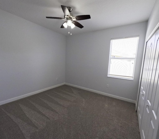 empty room featuring a ceiling fan, baseboards, and dark carpet