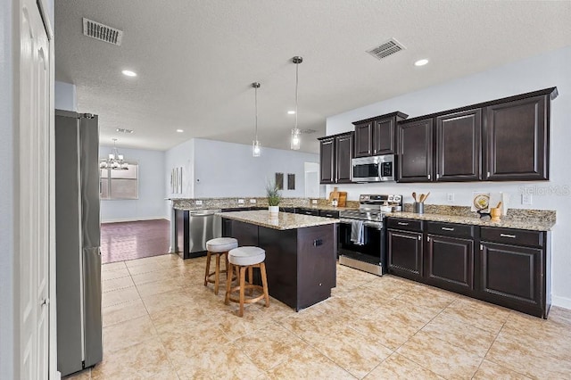 18677 Milton Keynes Ct, Land O Lakes, FL 34638 - kitchen with appliances with stainless steel finishes, a peninsula, a kitchen breakfast bar, decorative light fixtures, and light stone countertops