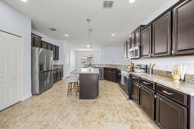 18677 Milton Keynes Ct, Land O Lakes, FL 34638 - kitchen with appliances with stainless steel finishes, a breakfast bar area, light stone counters, dark brown cabinets, and a kitchen island