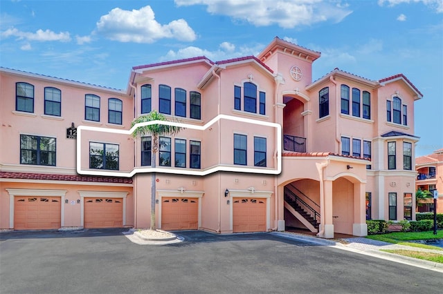 view of front of home with an attached garage, stucco siding, a tiled roof, and stairway