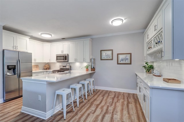 kitchen with a peninsula, a breakfast bar, light wood-style floors, tasteful backsplash, and appliances with stainless steel finishes