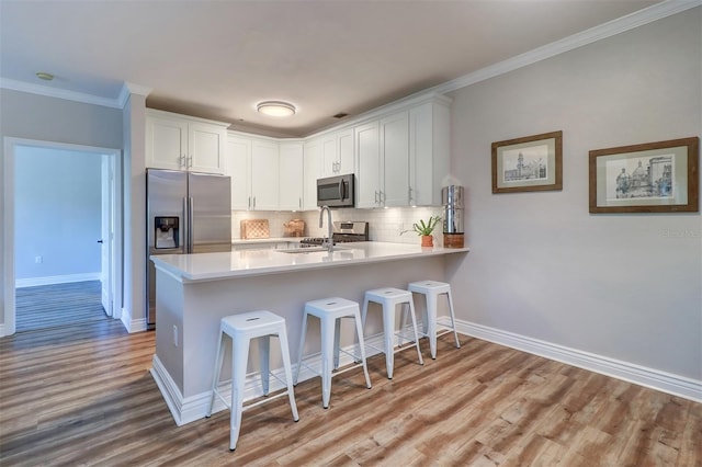 kitchen featuring backsplash, a sink, light wood finished floors, a peninsula, and stainless steel appliances