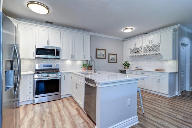 kitchen with a peninsula, light wood-style floors, a sink, appliances with stainless steel finishes, and backsplash