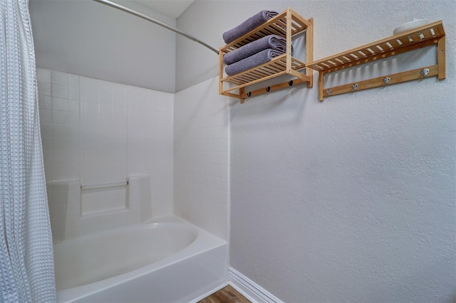 bathroom with baseboards, a textured wall, and shower / bath combo