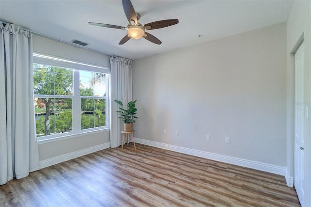 empty room featuring visible vents, a ceiling fan, baseboards, and wood finished floors