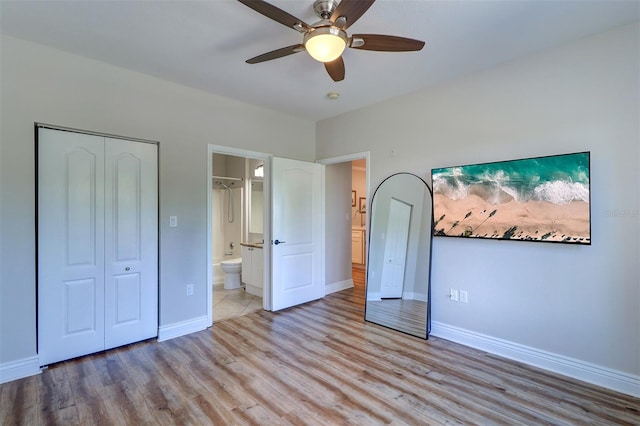 unfurnished bedroom featuring a ceiling fan, light wood-type flooring, baseboards, a closet, and ensuite bath