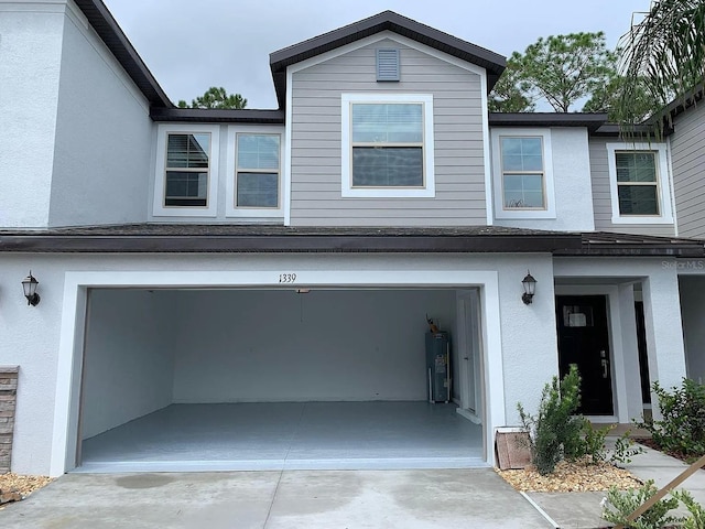view of front of house with a garage, stucco siding, water heater, and concrete driveway