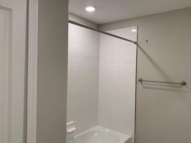 bathroom with a textured wall and washtub / shower combination