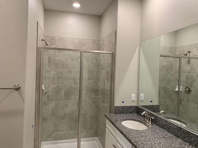 full bathroom featuring vanity, a textured wall, and a stall shower