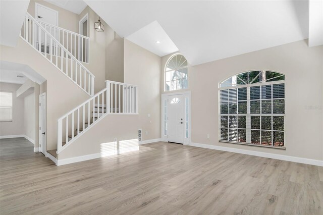 entryway featuring baseboards, a towering ceiling, wood finished floors, and stairway