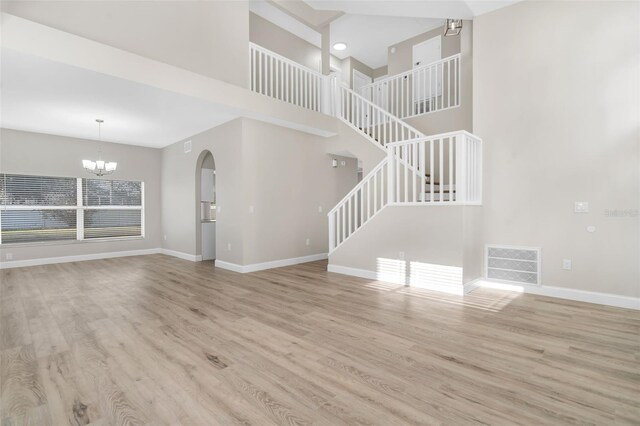 unfurnished living room featuring visible vents, wood finished floors, baseboards, a chandelier, and stairs