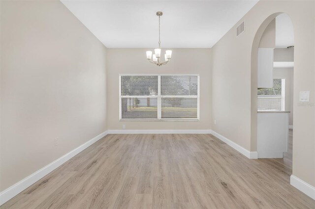 unfurnished dining area with visible vents, arched walkways, baseboards, light wood finished floors, and a chandelier