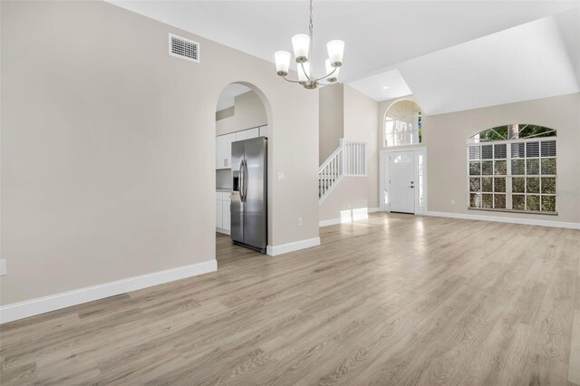 unfurnished living room with visible vents, arched walkways, light wood-style floors, and an inviting chandelier