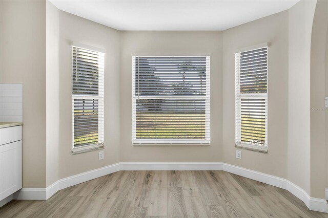 unfurnished dining area featuring baseboards, a healthy amount of sunlight, and light wood finished floors