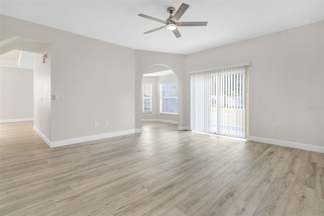 spare room featuring baseboards, a ceiling fan, light wood finished floors, and arched walkways