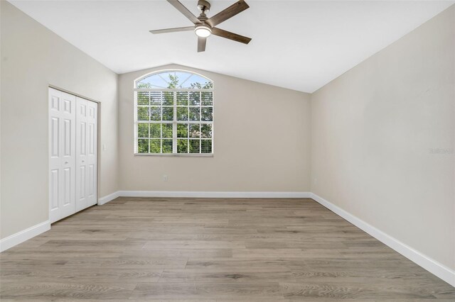 unfurnished bedroom featuring baseboards, light wood finished floors, lofted ceiling, and a closet