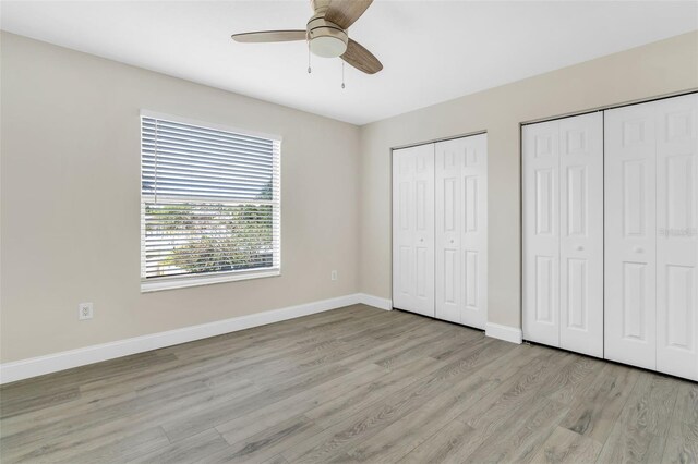 unfurnished bedroom with a ceiling fan, baseboards, multiple closets, and light wood-style floors