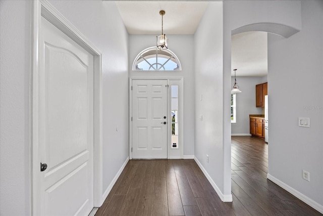 foyer entrance with arched walkways, baseboards, dark wood finished floors, and plenty of natural light