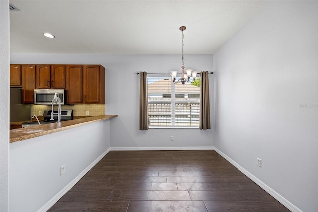 kitchen featuring stainless steel appliances, tasteful backsplash, dark wood-type flooring, an inviting chandelier, and baseboards