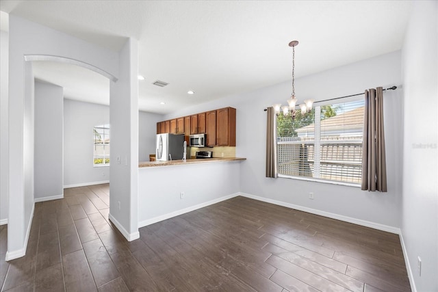 kitchen with brown cabinets, a notable chandelier, dark wood finished floors, arched walkways, and appliances with stainless steel finishes