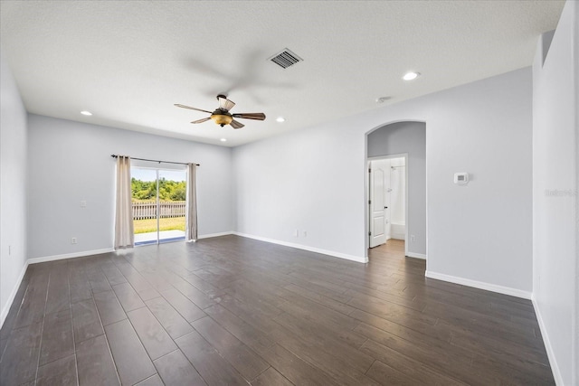 spare room featuring visible vents, ceiling fan, arched walkways, dark wood-style floors, and baseboards