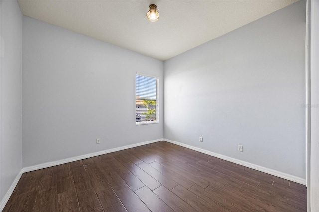 spare room with baseboards and dark wood-style floors