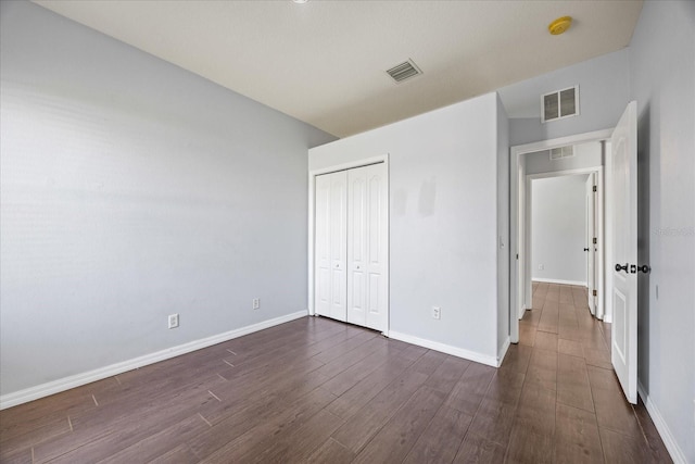 unfurnished bedroom with a closet, visible vents, dark wood-style flooring, and baseboards