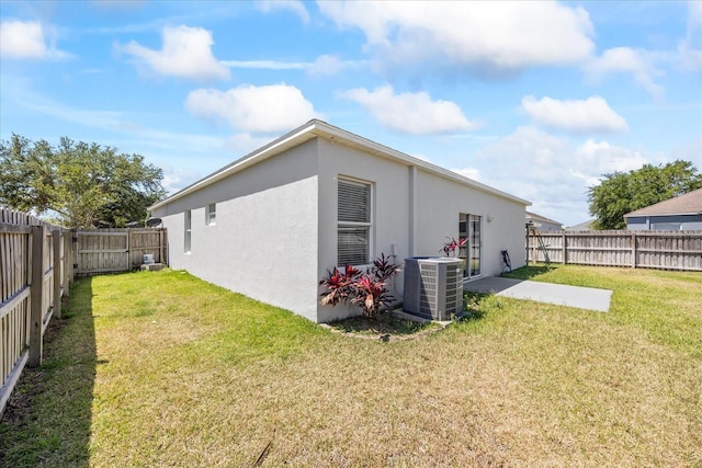 back of house featuring a yard, a fenced backyard, stucco siding, and central AC