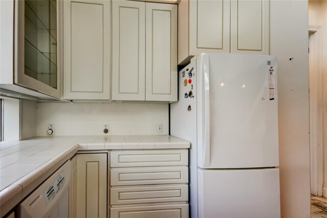 919 Sandpiper Way S, Saint Petersburg, FL 33707 - kitchen featuring cream cabinetry, white appliances, tile counters, and glass insert cabinets