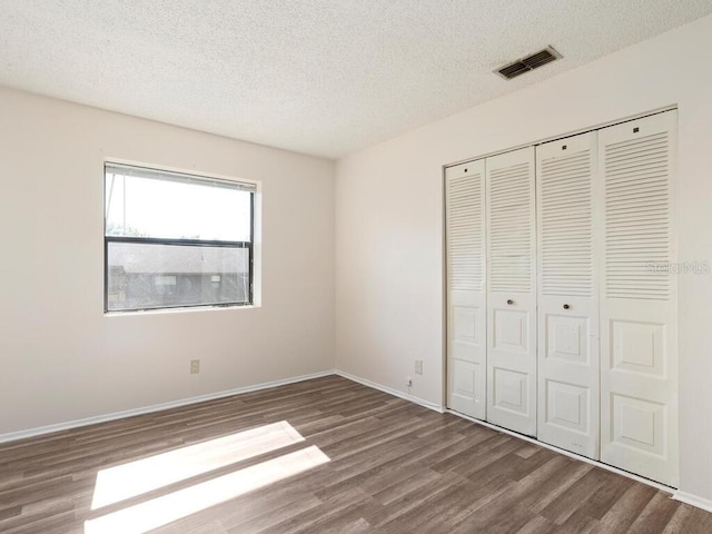 unfurnished bedroom featuring a textured ceiling, a closet, visible vents, and wood finished floors