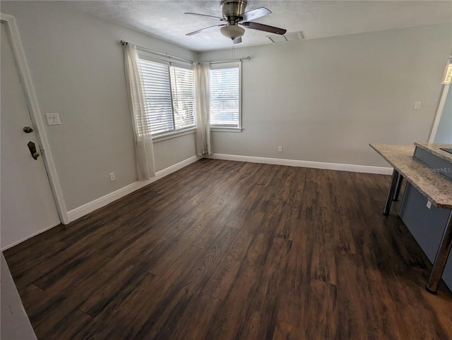 unfurnished dining area with dark wood-type flooring, a ceiling fan, baseboards, and a textured ceiling