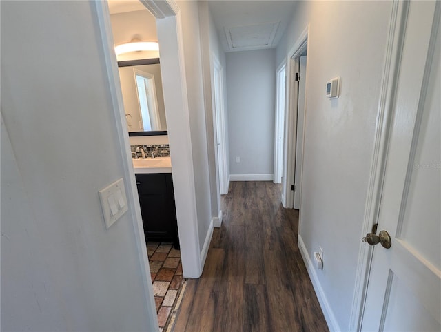 hallway with dark wood-style flooring, attic access, baseboards, and a sink