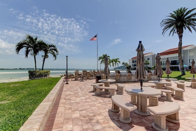 view of community with a yard, exterior kitchen, a water view, and a patio area
