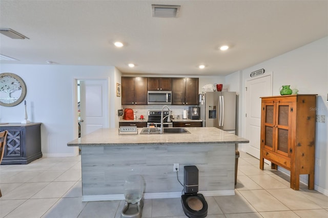 kitchen featuring a sink, an island with sink, dark brown cabinetry, backsplash, and appliances with stainless steel finishes