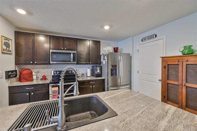 kitchen with a sink, stainless steel appliances, tasteful backsplash, dark brown cabinetry, and light countertops