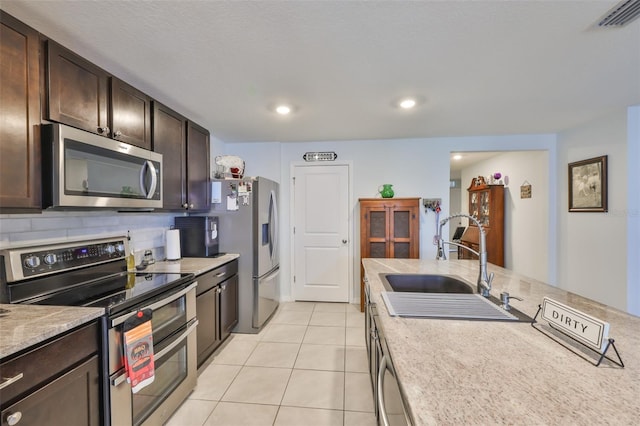 kitchen featuring dark brown cabinets, a sink, stainless steel appliances, light countertops, and tasteful backsplash
