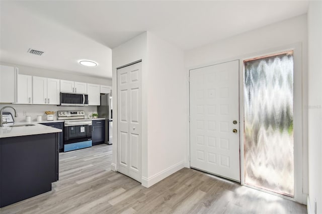 2953 Yucca Ct, Palm Harbor, FL 34684 - kitchen featuring appliances with stainless steel finishes, a sink, light wood-style flooring, white cabinetry, and light countertops