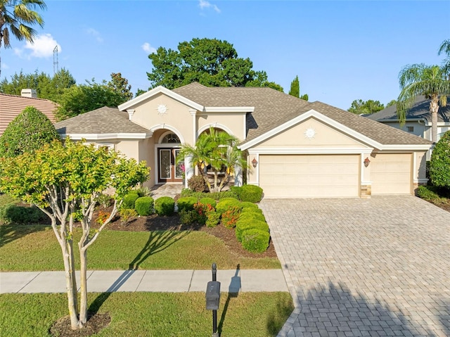 view of front facade featuring a front yard, stucco siding, decorative driveway, and a garage