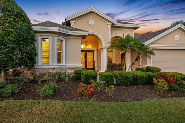 view of front of house with an attached garage, stucco siding, french doors, and stone siding