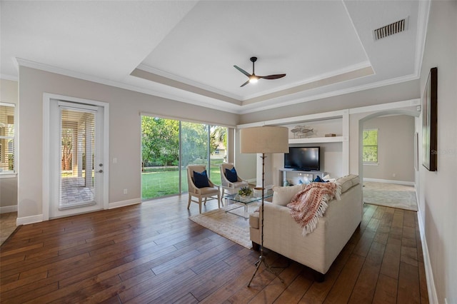 living room featuring visible vents, dark wood-style flooring, a ceiling fan, a tray ceiling, and baseboards