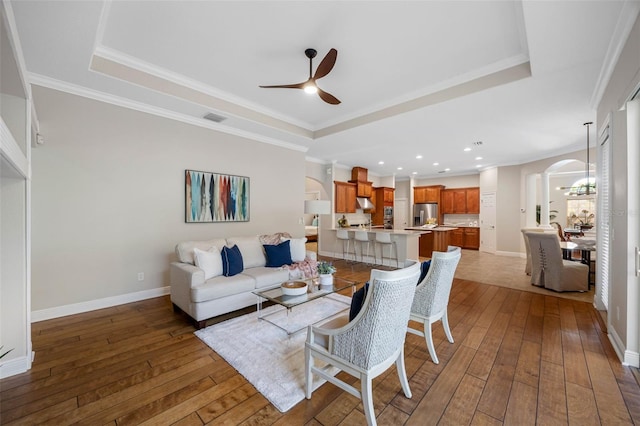 living room featuring ceiling fan with notable chandelier, visible vents, wood-type flooring, arched walkways, and a raised ceiling
