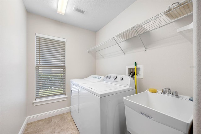 washroom featuring laundry area, baseboards, light tile patterned floors, a sink, and separate washer and dryer
